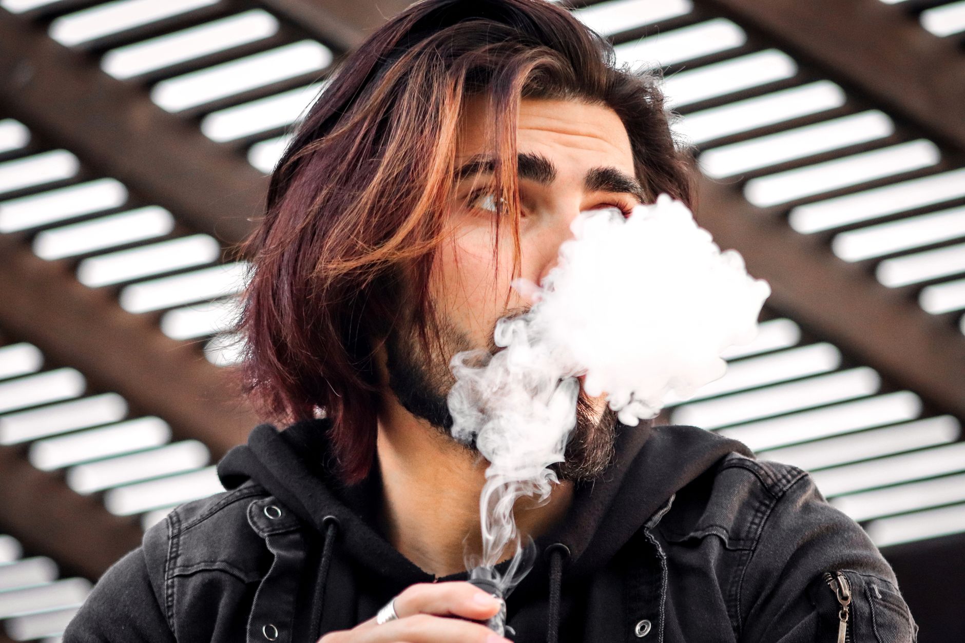 Gros plan d'un homme élégant vapotant à l'extérieur, créant d'épais nuages de vapeur.