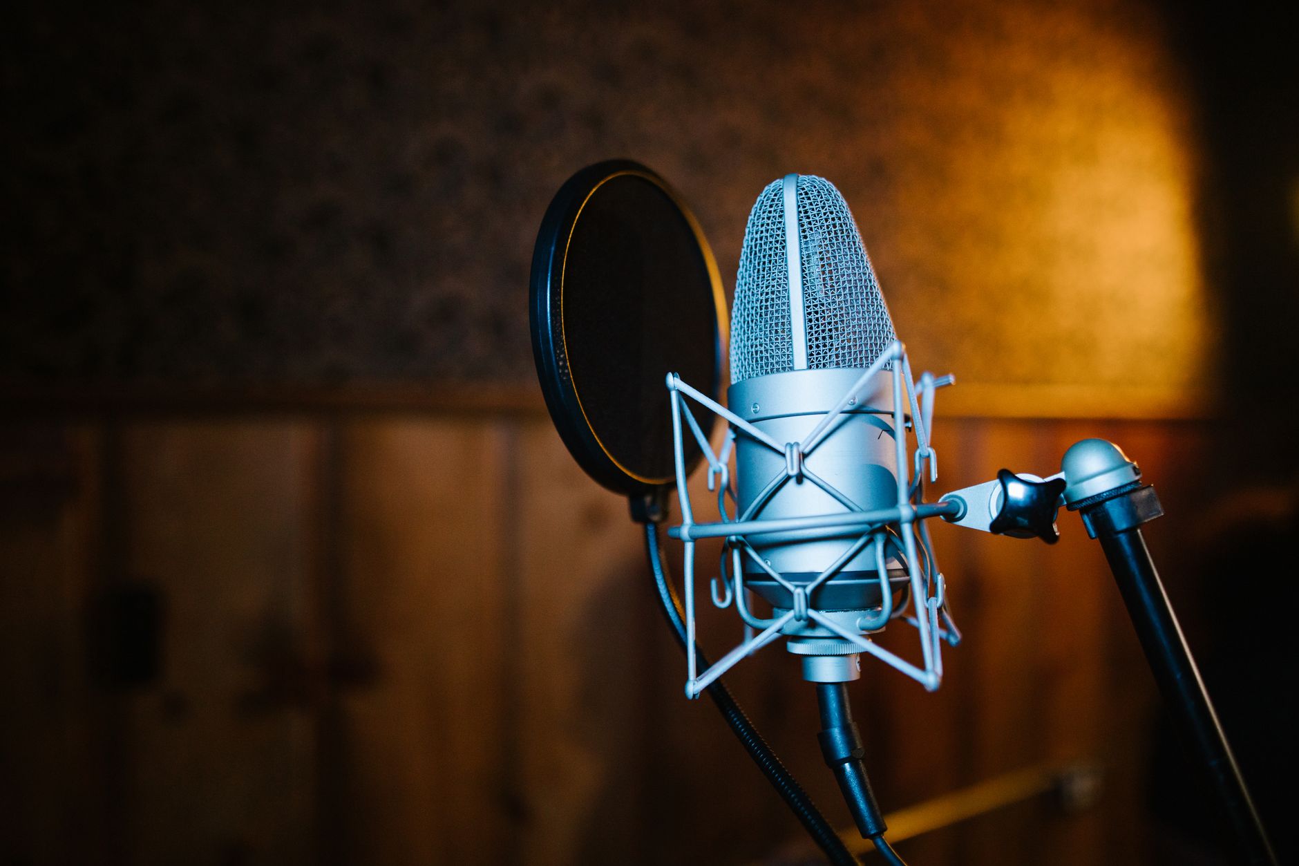 Microphone de studio argenté avec suspension et filtre anti-pop devant un mur en bois éclairé d’une lumière chaude.